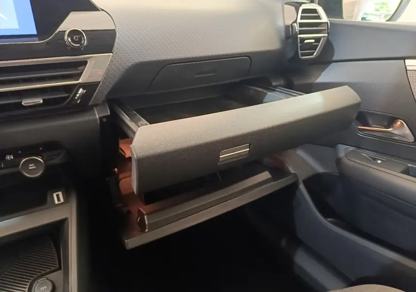 Vue intérieure côté passager du tableau de bord noir du Citroën C4 X avec boîte à gants ouverte et détails de la console.