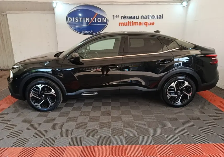 Profil côté gauche d'une Citroën C4 X noire 2023, avec jantes distinctives et toit panoramique en intérieur showroom.