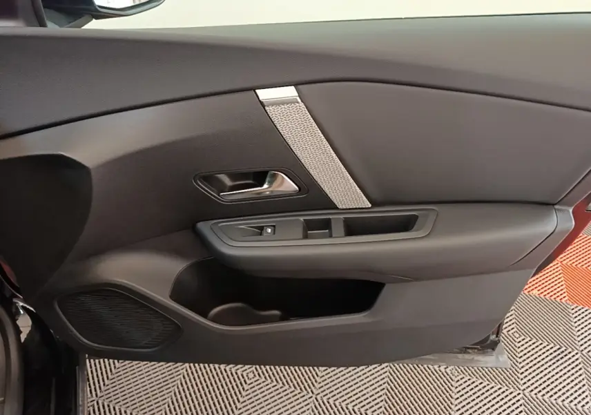 Intérieur côté gauche de la porte noire du Citroën C4 X 2023 avec poignée chromée et haut-parleur intégré.