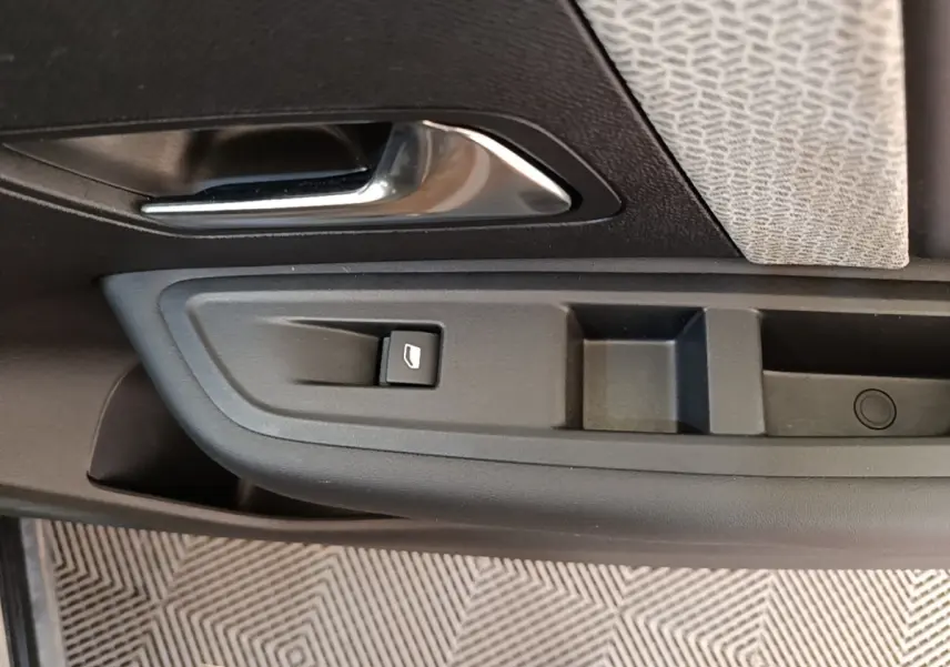 Gros plan sur la poignée intérieure et commande de vitre côté gauche d’une Citroën C4 X noire, finition 2023.