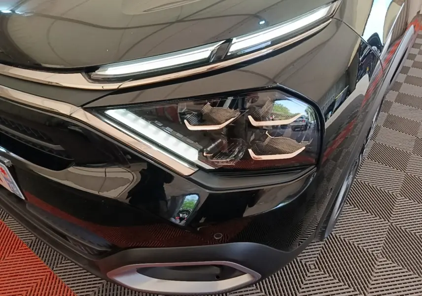 Gros plan sur le phare avant droit noir brillant du Citroën C4 X 2023 avec détails LED et calandre chromée.