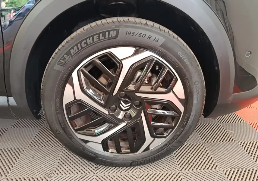 Gros plan sur la roue avant droite noire d'une Citroën C4 X 2023 avec jante alliage au design géométrique.