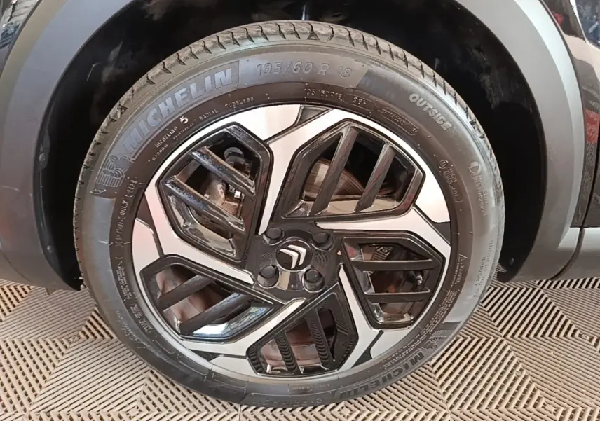 Gros plan sur la roue avant gauche noire d'une Citroën C4 X 2023 avec jante alliage bicolore et pneu Michelin.