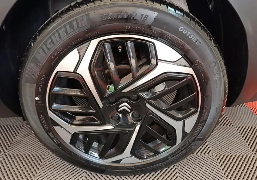 Gros plan sur la roue avant gauche noire avec jante alliage bicolore et logo Citroën au centre.