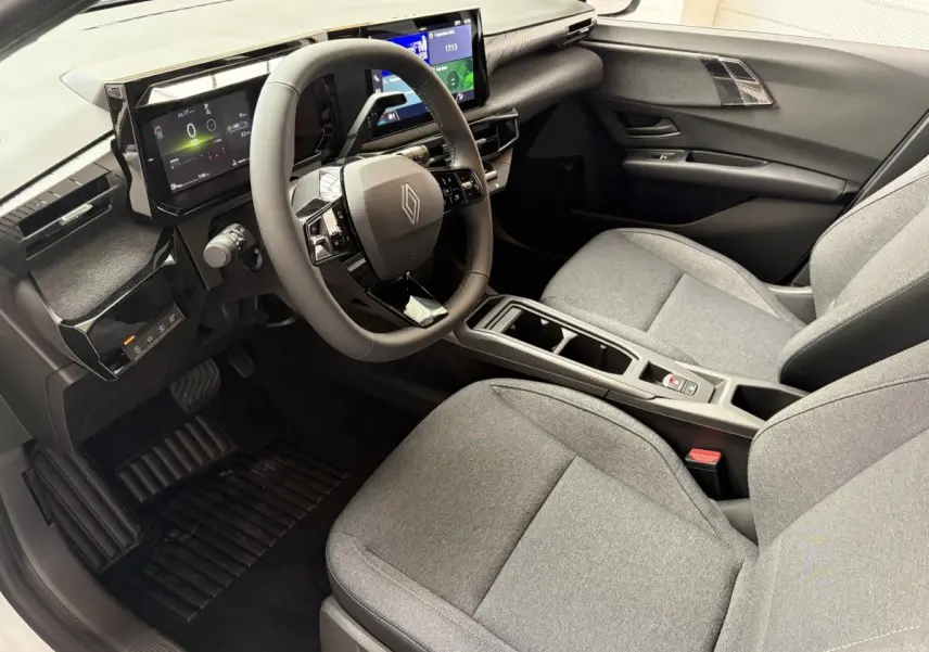Intérieur de la Renault Clio 2026 blanc, vue côté conducteur, tableau de bord numérique et sièges gris tissu.