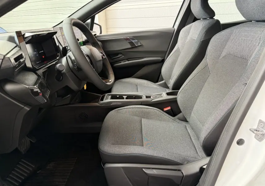 Intérieur avant droit de la Renault Clio 2026 blanche, sièges tissu gris et tableau de bord moderne avec écran tactile.