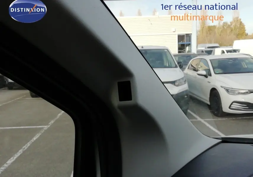Vue intérieure côté gauche du pare-brise d'un Citroën Berlingo XL blanc Icy, avec parking et autres véhicules en arrière-plan.
