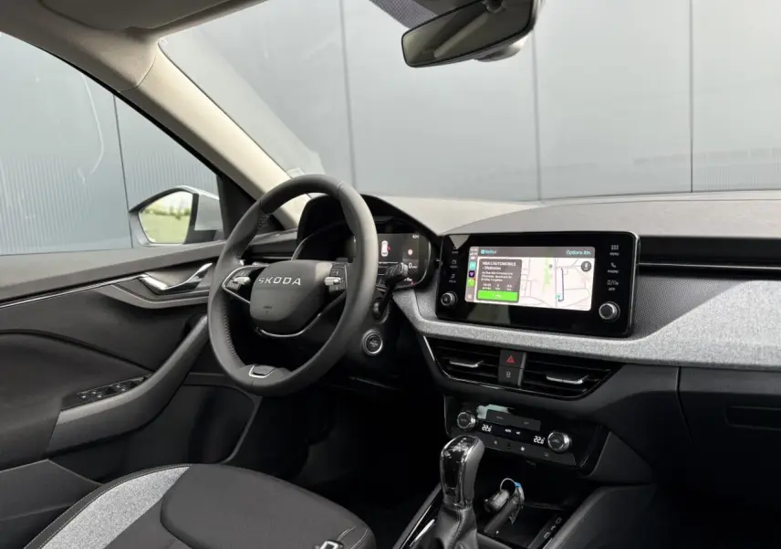 Intérieur avant droit du Skoda Kamiq 2025, tableau de bord gris clair avec écran tactile et volant multifonctions noir.