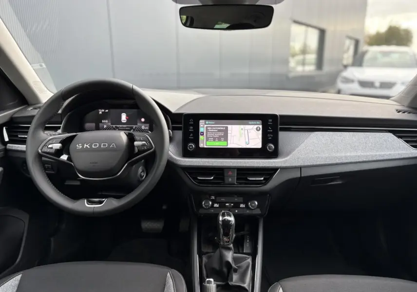Intérieur du Skoda Kamiq 2025 vu de face, tableau de bord gris clair avec écran tactile et volant multifonctions noir.