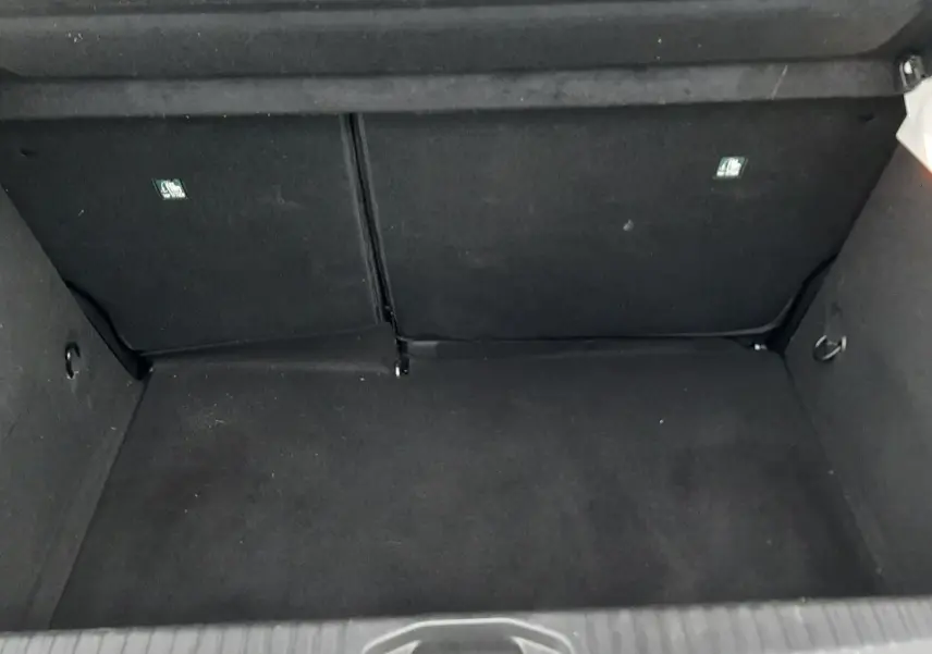 Vue intérieure du coffre vide de la Renault Clio V blanche, montrant le revêtement noir et la banquette arrière rabattue partiellement.