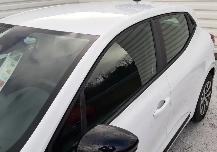 Vue 3/4 avant droit d'une Renault Clio V blanche avec rétroviseur noir et vitres teintées.