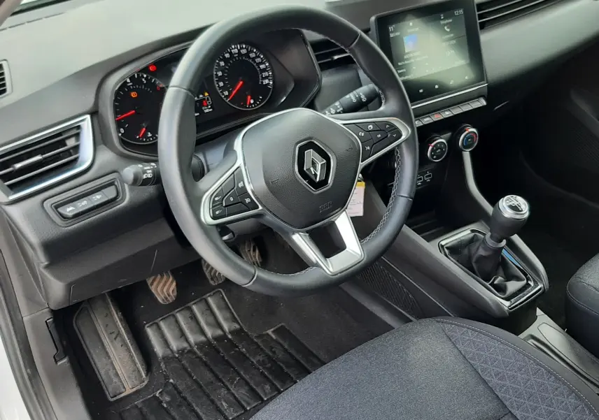 Vue intérieure côté conducteur de la Renault Clio V blanche, montrant le volant multifonction et la boîte manuelle.