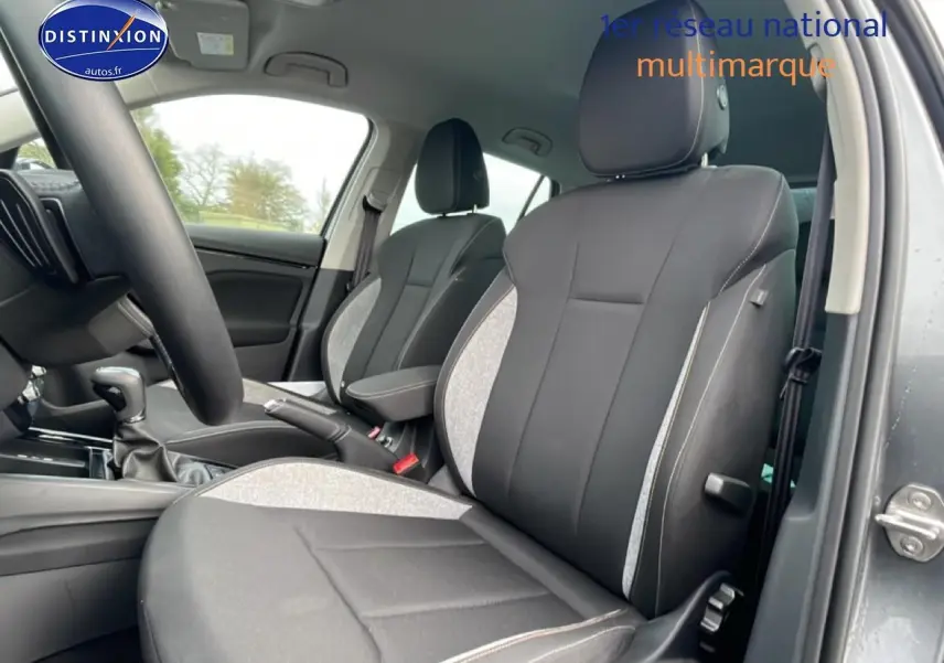 Vue intérieure côté avant droit du Skoda Kamiq gris, mettant en valeur les sièges bi-matière et l'accoudoir central.