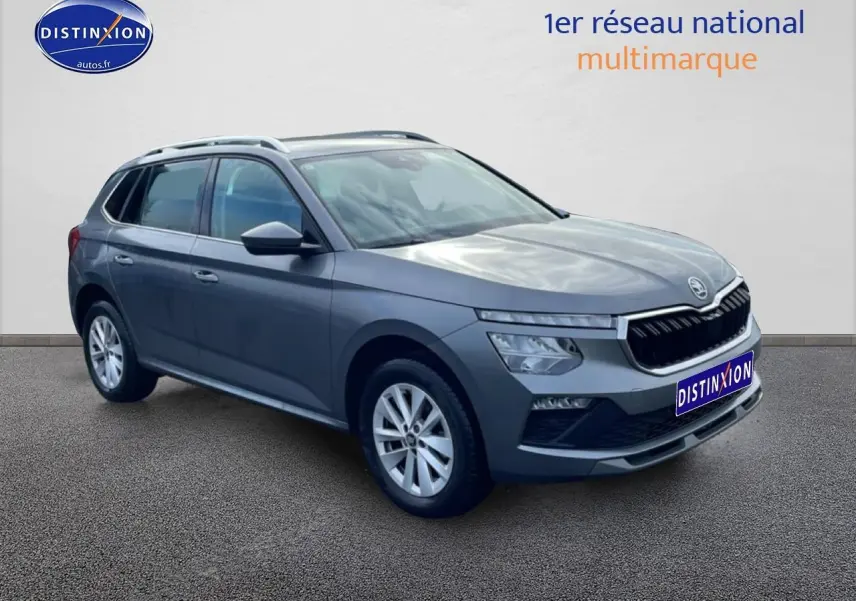 SUV Skoda Kamiq gris en 3/4 avant droit avec calandre chromée et barres de toit visibles.