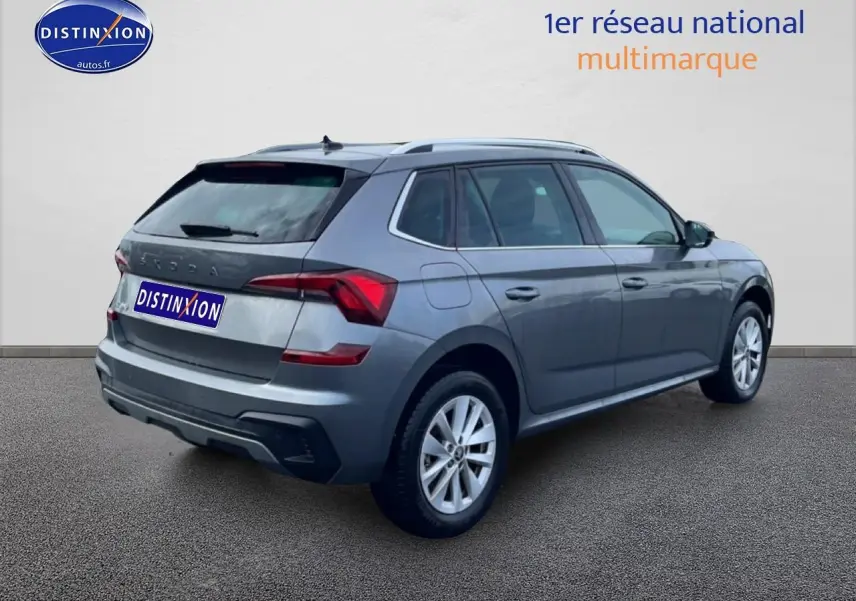 Vue 3/4 arrière droite d'un Skoda Kamiq gris avec barres de toit et jantes alu sur fond neutre.