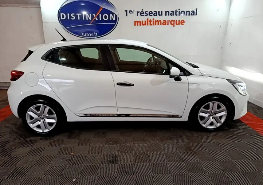 Profil droit d'une Renault Clio Business blanche de 2021, avec jantes alliage et rétroviseurs blancs dans un showroom.