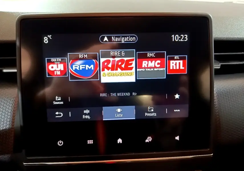 Écran tactile central du tableau de bord de la Renault Clio Business blanc, affichant les stations radio et la navigation.