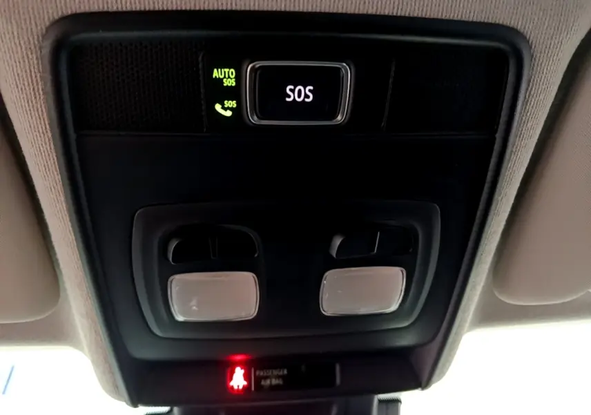 Vue en gros plan du plafonnier intérieur noir avec bouton SOS éclairé en vert et lampes de lecture dans une Renault Clio blanche.
