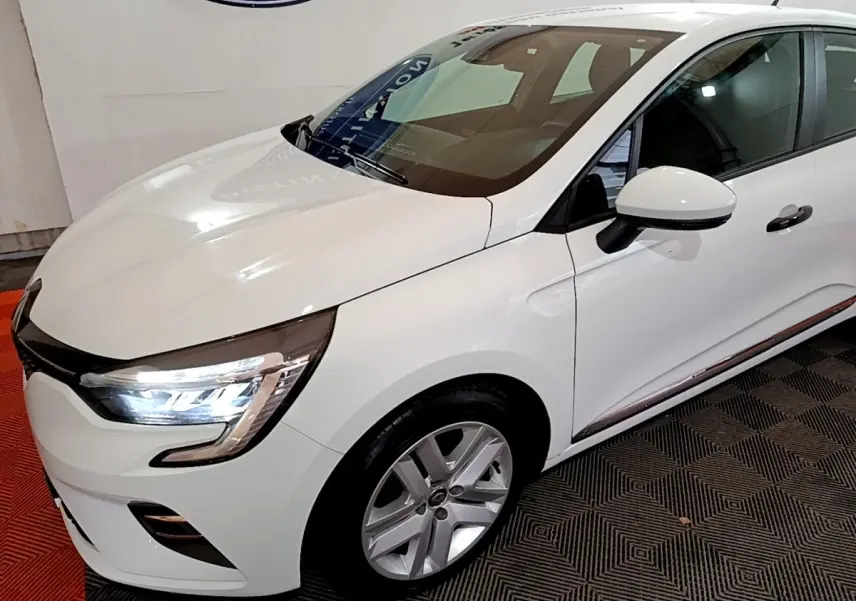 Vue 3/4 avant droit d'une Renault Clio Business blanche avec phares LED allumés et jantes alliage visibles.