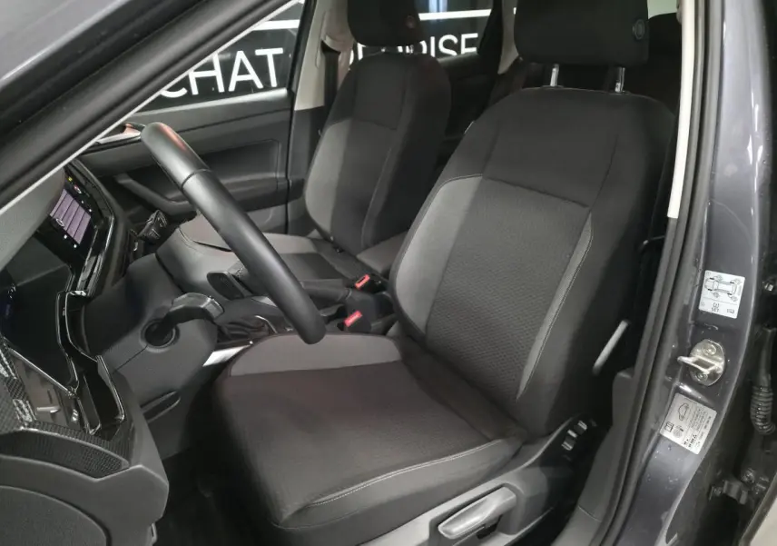 Vue intérieure côté conducteur de la Volkswagen Polo gris, montrant les sièges en tissu et le volant multifonction cuir.