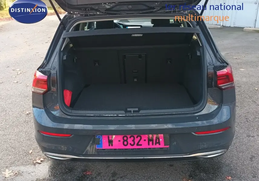 Vue arrière d'une Volkswagen Golf gris Urano 2024 avec coffre ouvert sur un parking extérieur.