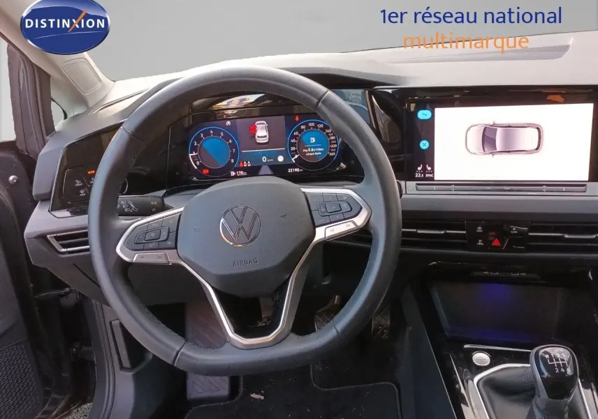 Vue intérieure centrée sur le volant et tableau de bord numérique d’une Volkswagen Golf gris Urano avec boîte manuelle.