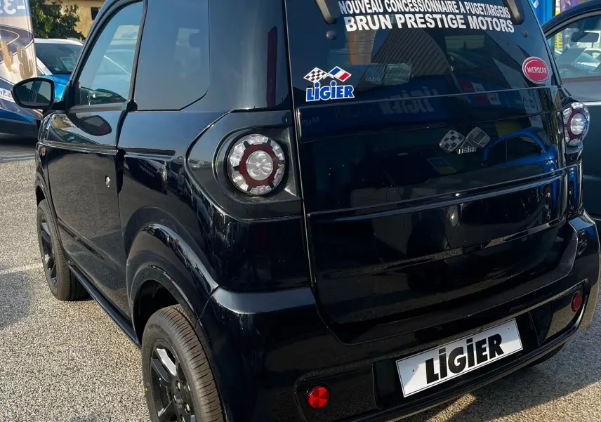 Vue 3/4 arrière droite d'une Ligier Myli électrique noire intense 2024 avec stickers concessionnaire sur la lunette arrière.