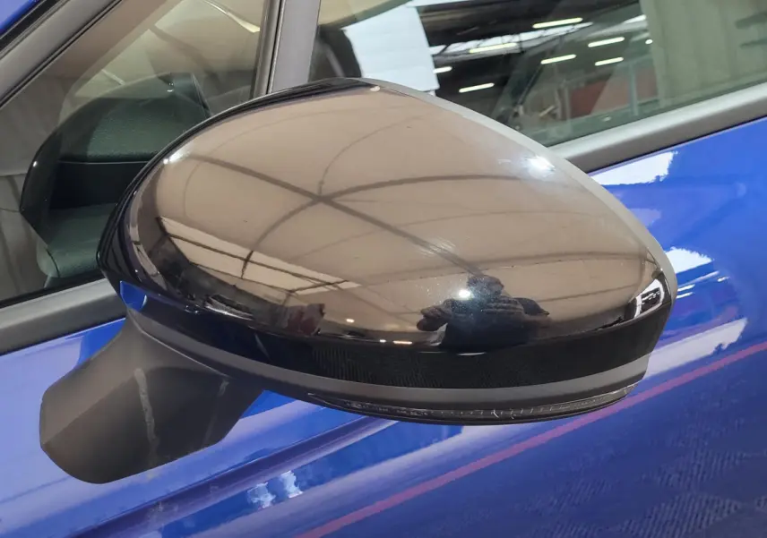 Rétroviseur extérieur droit noir brillant sur Renault Clio bleu, avec clignotant intégré visible de près.