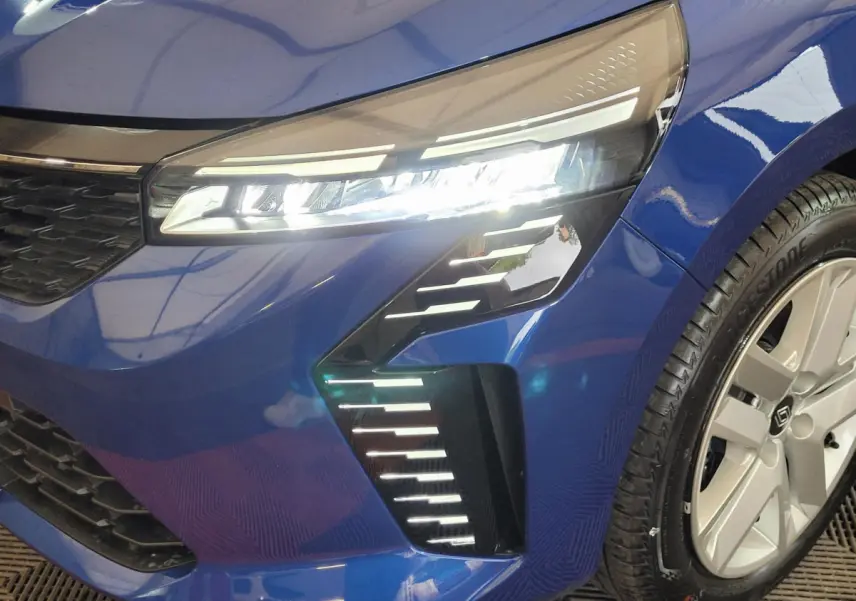 Gros plan sur l'avant droit bleu de la Renault Clio 2025 avec phares LED et jante alliage visible.