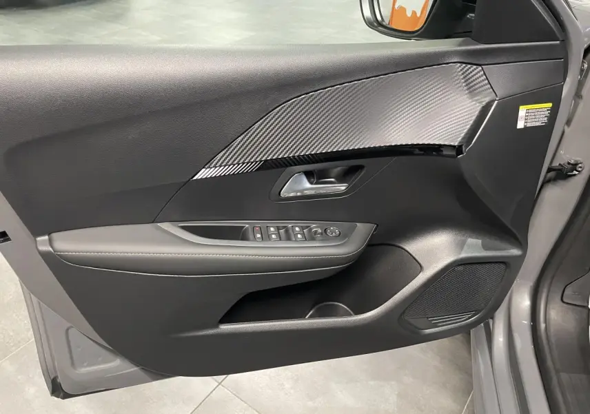 Vue intérieure de la porte avant gauche gris selenium de la Peugeot 208 avec insert décor carbone et commandes électriques.
