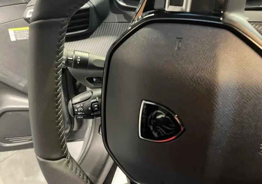Gros plan sur le volant cuir noir de la Peugeot 208 2025 avec commandes multimédia et logo lion central.