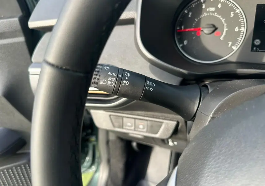 Gros plan sur la manette de phares et clignotants à gauche du volant dans l'habitacle d'une Dacia Sandero Stepway.