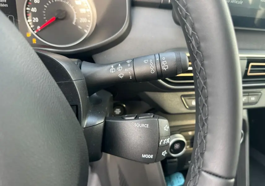Gros plan sur la commande au volant côté gauche d'une Dacia Sandero III Stepway, intérieur noir avec tableau de bord numérique.