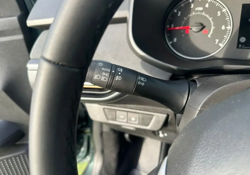 Gros plan sur la manette de commande des phares et clignotants côté gauche du volant dans l’habitacle noir du Dacia Sandero Vert Cèdre.