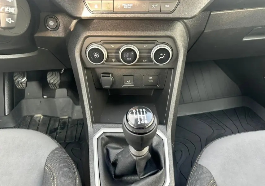 Vue intérieure centrée sur le levier de vitesses manuel de la Dacia Sandero III Stepway, avec commandes climatisation et pédales visibles.