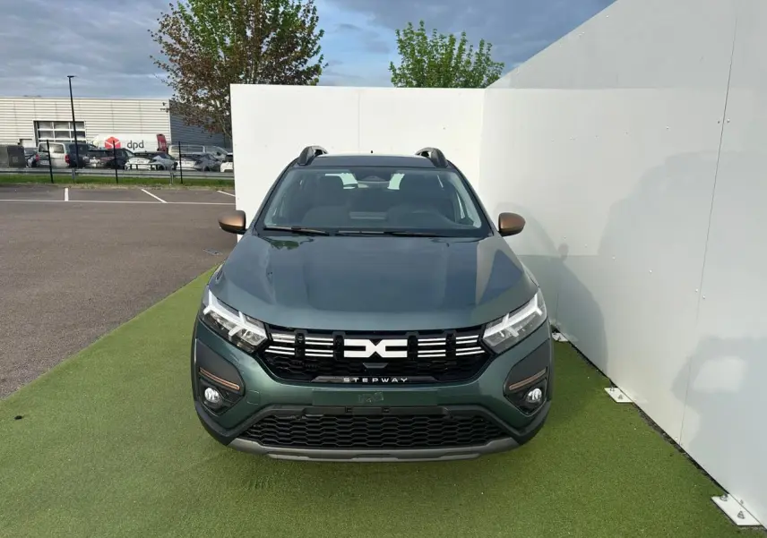 Vue avant d'une Dacia Sandero III Stepway 2025 vert cèdre avec calandre noire et barres de toit grises.