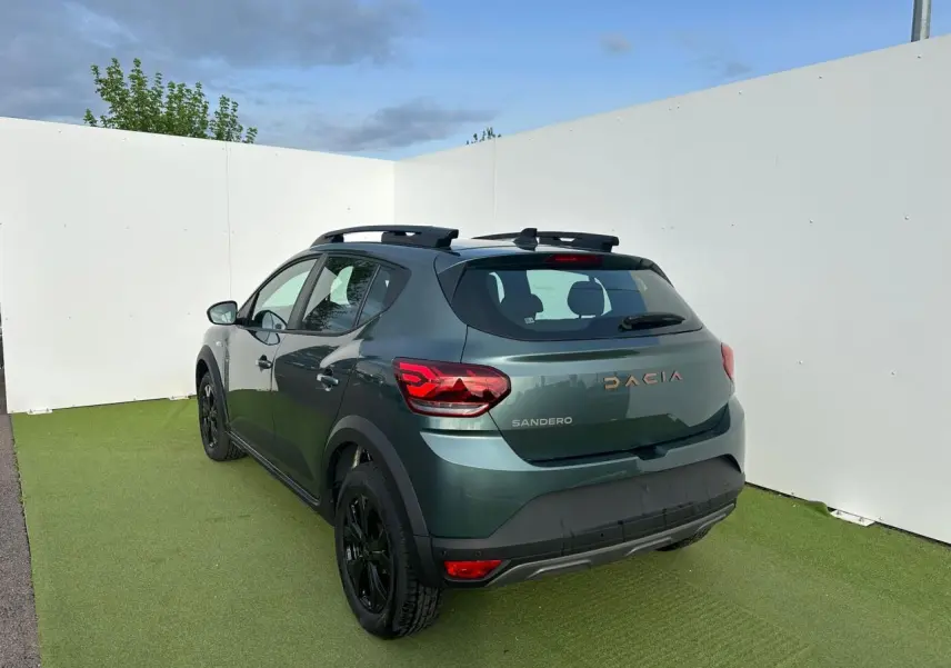 Vue 3/4 arrière droite de la Dacia Sandero III Stepway vert cèdre avec jantes noires et barres de toit.