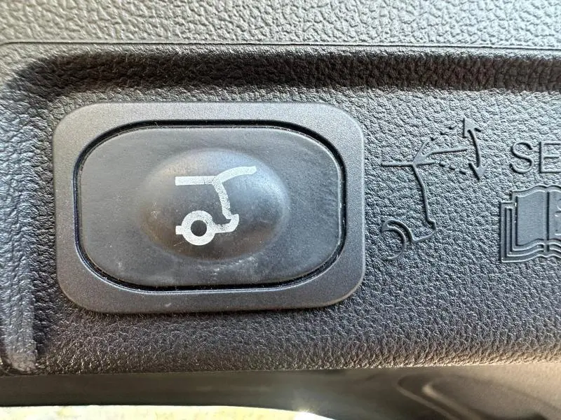 Bouton noir de commande d'ouverture du hayon sur Ford Puma 1.0 EcoBoost 155ch mHEV ST-Line gris Solar métallisé, vue rapprochée intérieure.