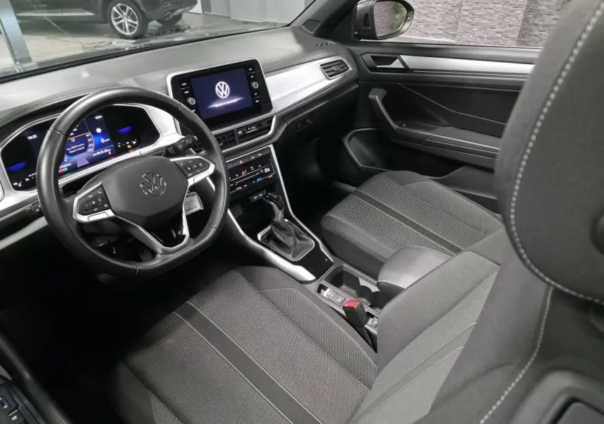 Vue intérieure côté conducteur du Volkswagen T-Roc Cabriolet 2024, sellerie tissu noire et tableau de bord moderne.