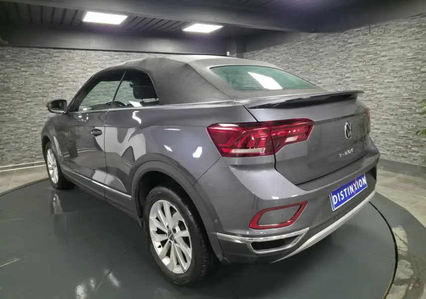Vue 3/4 arrière droite du Volkswagen T-Roc Cabriolet gris métallisé avec capote noire en intérieur showroom.