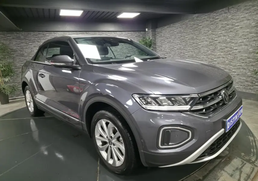Volkswagen T-Roc cabriolet gris métallisé en 3/4 avant droit dans un showroom avec capote noire fermée.