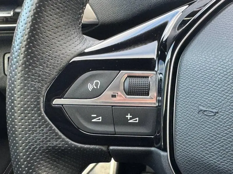 Gros plan sur les commandes gauche du volant noir du Peugeot 3008 2024, avec molette et boutons de réglage audio.