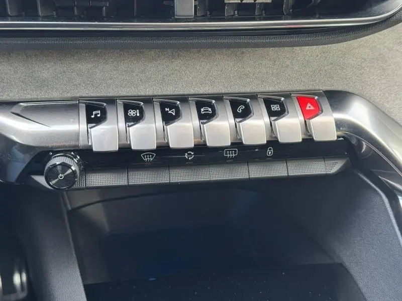 Gros plan sur les commandes centrales argentées et noires du tableau de bord du Peugeot 3008 noir 2024, avec bouton rouge d’alerte.