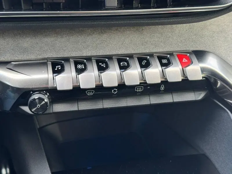 Gros plan sur la rangée de boutons argentés et noirs du tableau de bord du Peugeot 3008 2024, avec bouton d’alerte rouge.