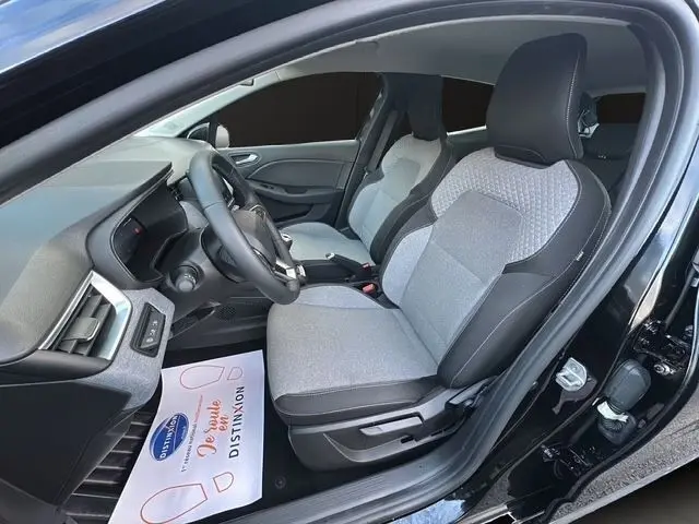 Vue intérieure côté conducteur de la Renault Clio noire 2025, sièges tissu gris avec contours noirs et volant multifonctions cuir synthétique.
