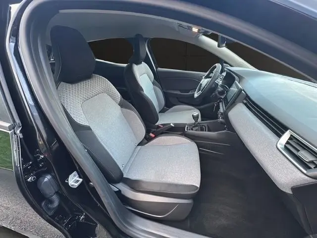 Vue intérieure côté conducteur de la Renault Clio noire 2025, sièges tissu gris clair et tableau de bord moderne.