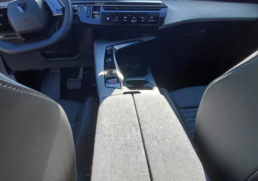 Vue intérieure du Peugeot 5008 Hybrid 2025 montrant la console centrale en tissu gris et le volant compact multifonction.