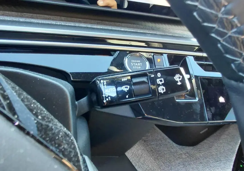 Gros plan sur la commande d’essuie-glace et le bouton start/stop dans l’habitacle noir du Peugeot 5008 Hybrid 2025.