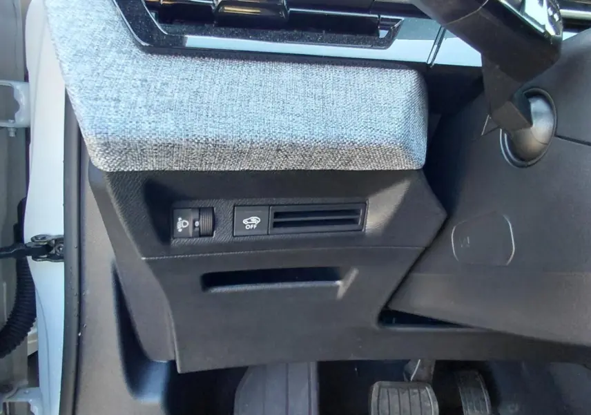 Détail de la console côté gauche sous le tableau de bord du Peugeot 5008 blanc Hybrid 2025 avec commandes et tissu gris.