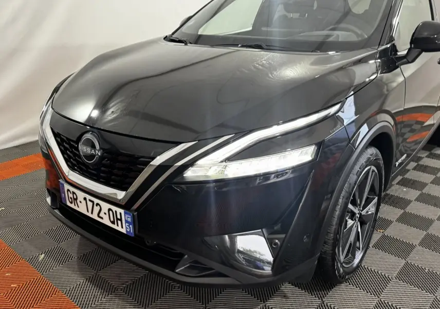 Vue 3/4 avant droit du Nissan Qashqai e-Power noir, avec calandre V-motion et phares LED allumés.